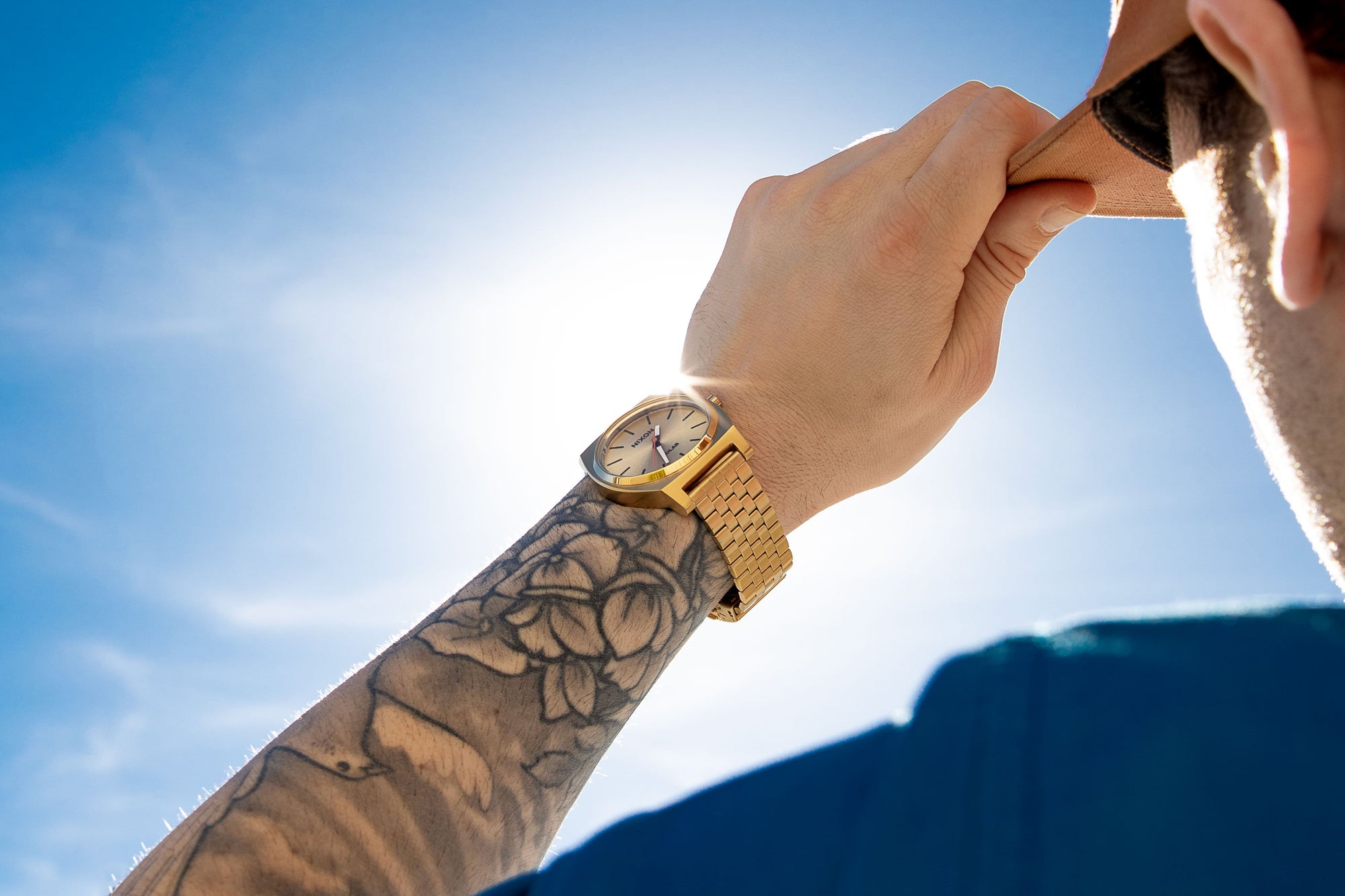 Man wears a gold Nixon Time Teller Solar watch while standing in the sun