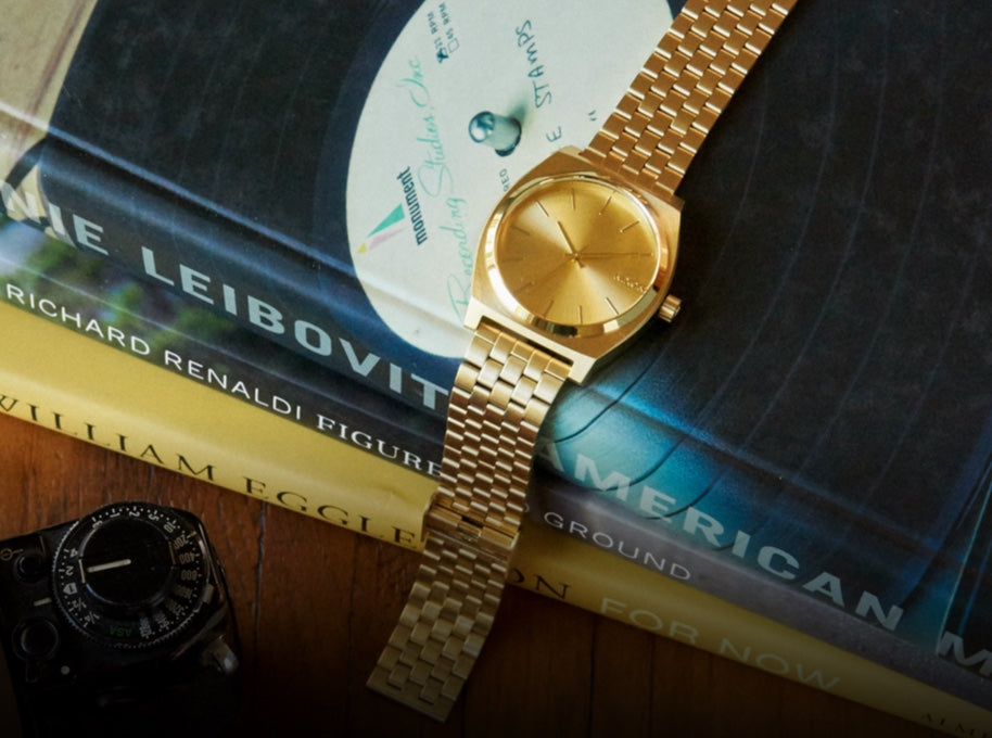 Gold Nixon Time Teller watch sitting across stack of books.