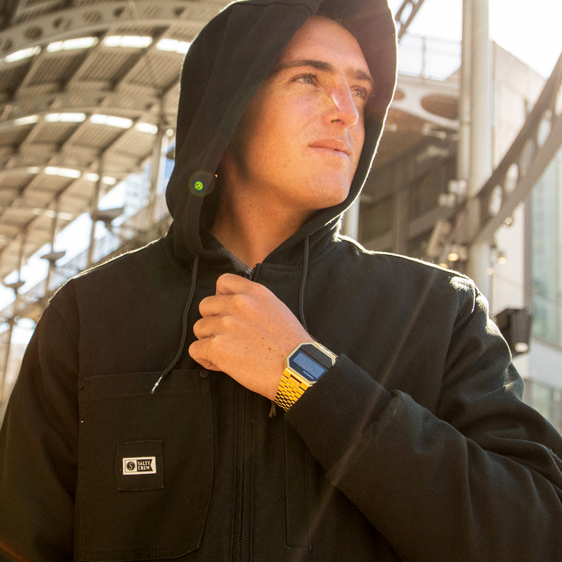 A man in a black hoodie shows off his gold Nixon Re-Run digital watch.