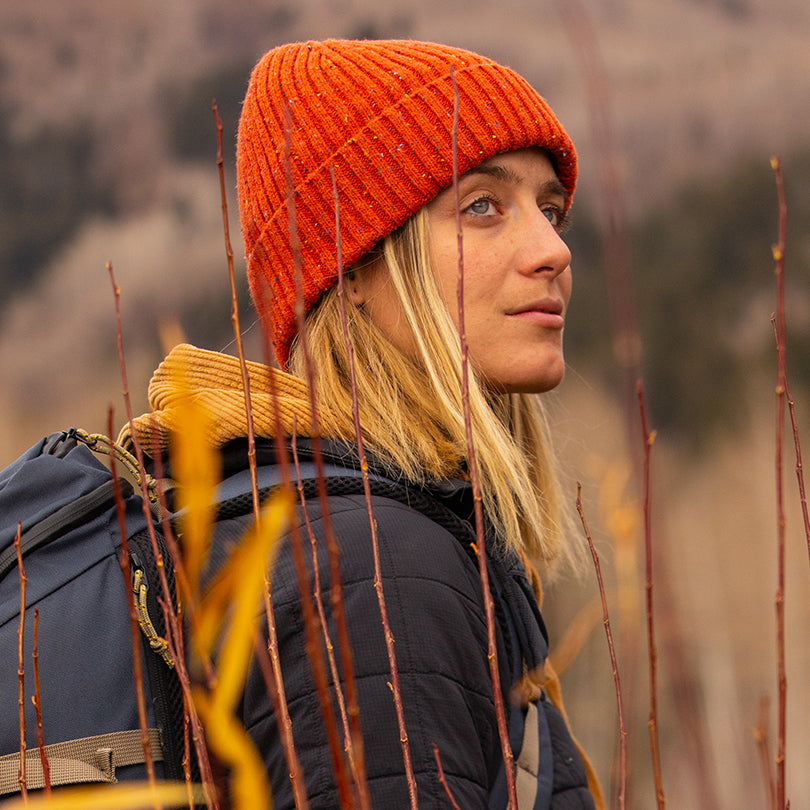 A woman wearing an orange Nixon beanie goes hiking outdoors.