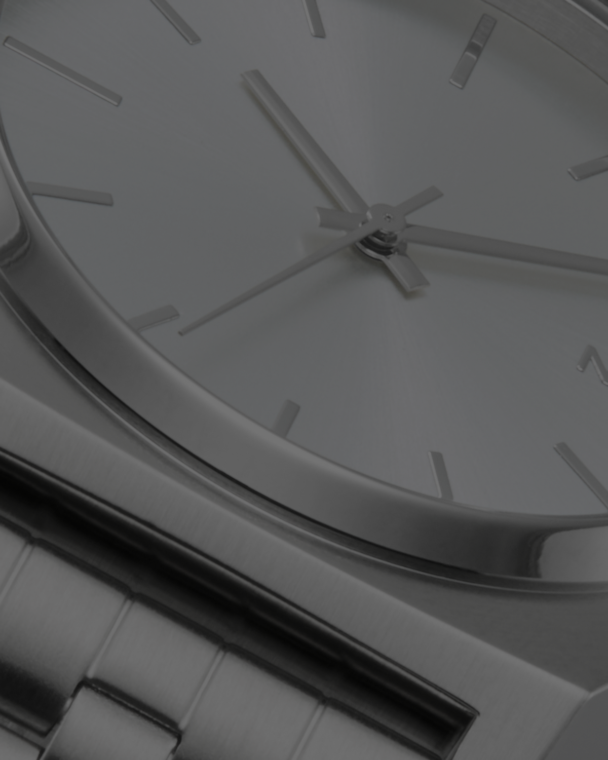 Close-up of a minimalist analog watch with a silver dial, slim silver-tone hands, stick indices, and a brushed metal bracelet.